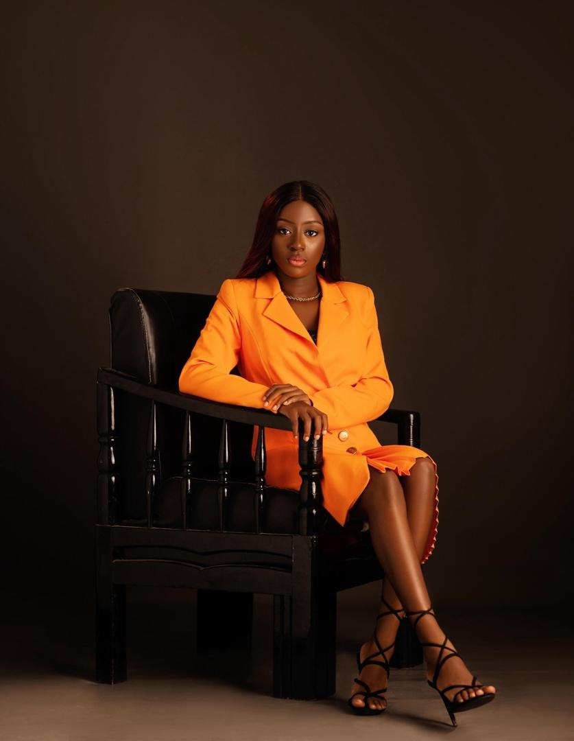Gesiere wearing an orange blazer, seated on a black chair